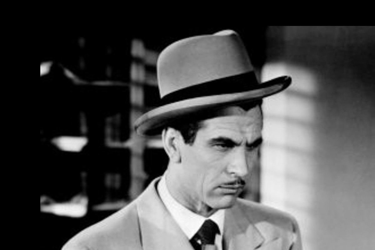 A man with a pencil-thin moustache and dressed in a grey suit and homburg inspects a piece of evidence.