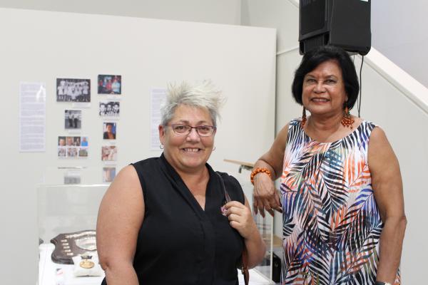 Two women standing in front of exhibition smiling at the camera